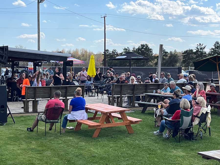 Ryders Roadhouse in Wisconsin Rapids Wisconsin People sit outdoors on benches and chairs, watching a performance on a sunny day.