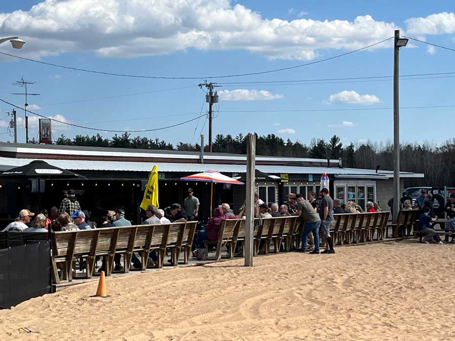 Ryders Roadhouse in Wisconsin Rapids Wisconsin People sit at long tables outside a beachside restaurant under a blue sky with scattered clouds.