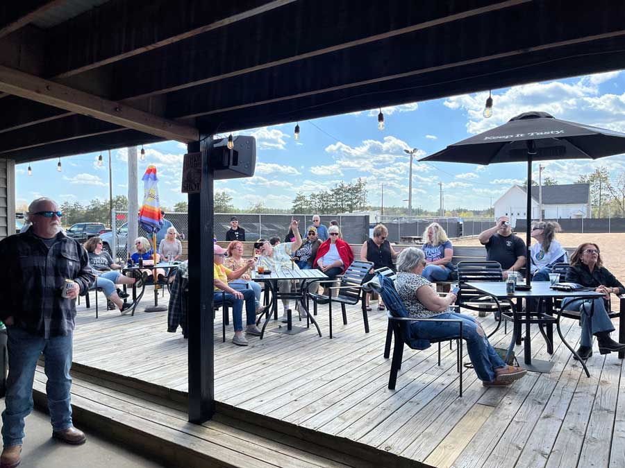Ryders Roadhouse in Wisconsin Rapids Wisconsin People sitting outdoors at tables on a wooden patio, enjoying sunny weather under string lights.