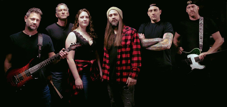 Ryders Roadhouse in Wisconsin Rapids Wisconsin Six band members pose together holding guitars and drumsticks against a black background.