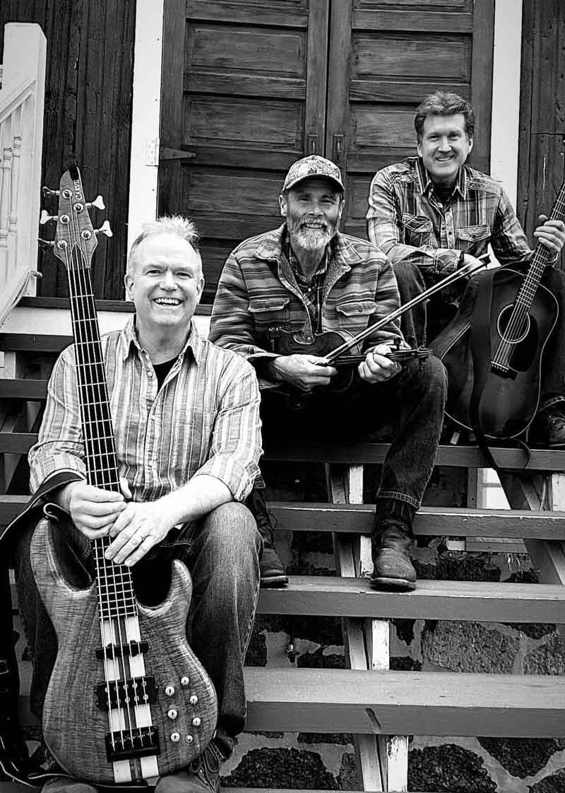 Ryders Roadhouse in Wisconsin Rapids Wisconsin Three smiling men with musical instruments sit on steps in front of a wooden door, black and white.